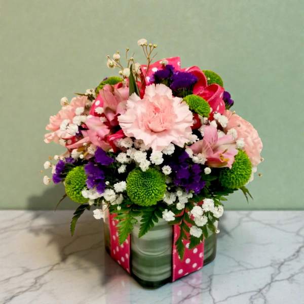 Mixed pink, purple, and green flower arrangement in a glass vase with a pink ribbon