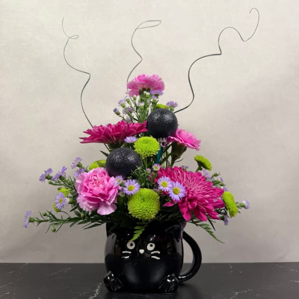Pink and purple flower arrangement in a black cat mug with curly wire accents