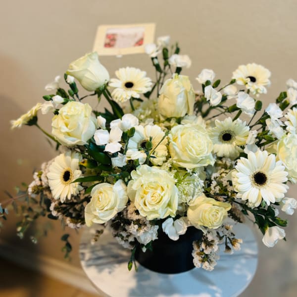 Cream roses and white daisies arranged in a black vase