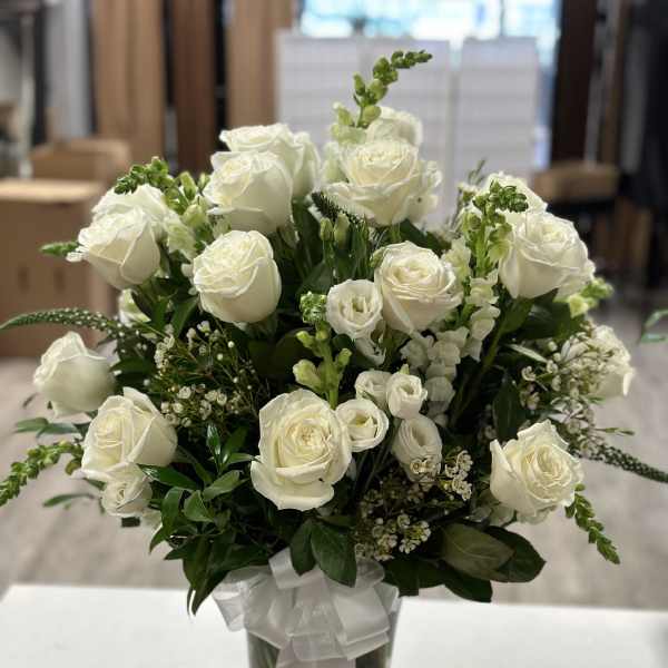 White rose bouquet in a clear glass vase with a white ribbon