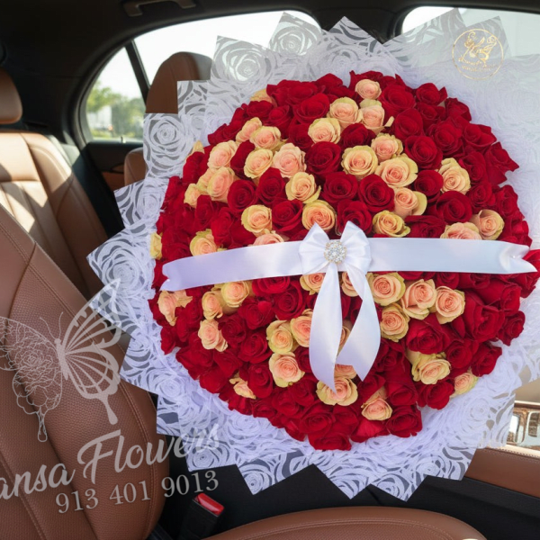 Large round bouquet of red and peach roses wrapped in white lace paper with a white ribbon bow