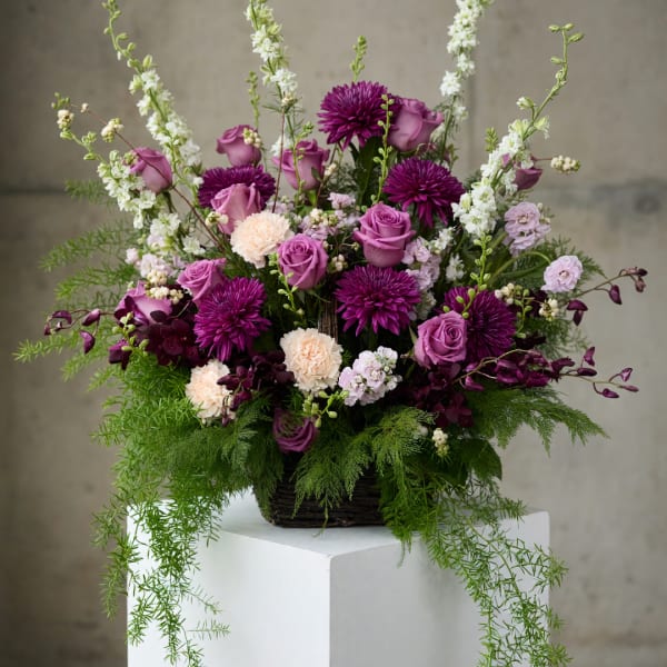 Purple and pink floral arrangement in a basket with trailing greenery