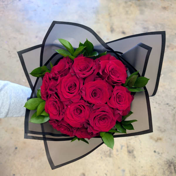 Bouquet of hot pink roses with green leaves wrapped in black-edged paper