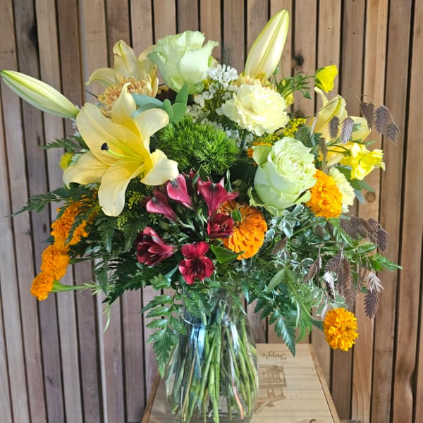 Mixed bouquet in a clear glass vase with lilies, roses, and orange blooms