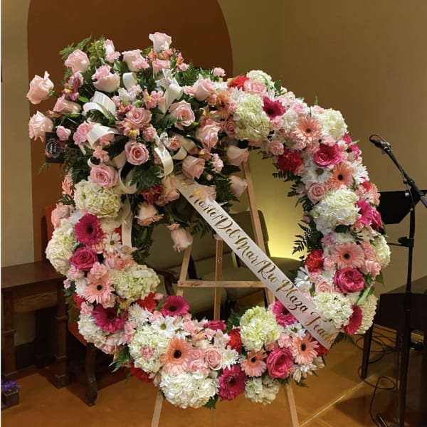 Large pink and white floral wreath on an easel with a memorial ribbon
