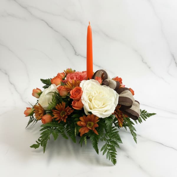 Orange floral centerpiece with a tall candle and ribbon bow