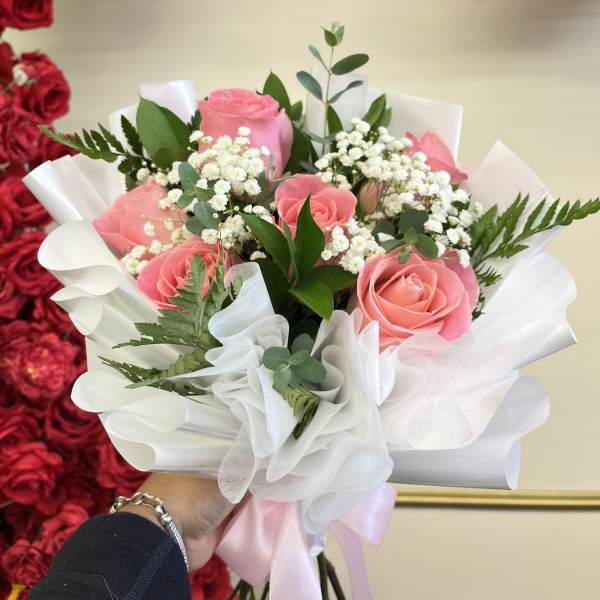 Pink roses in white wrapping with baby's breath and greenery