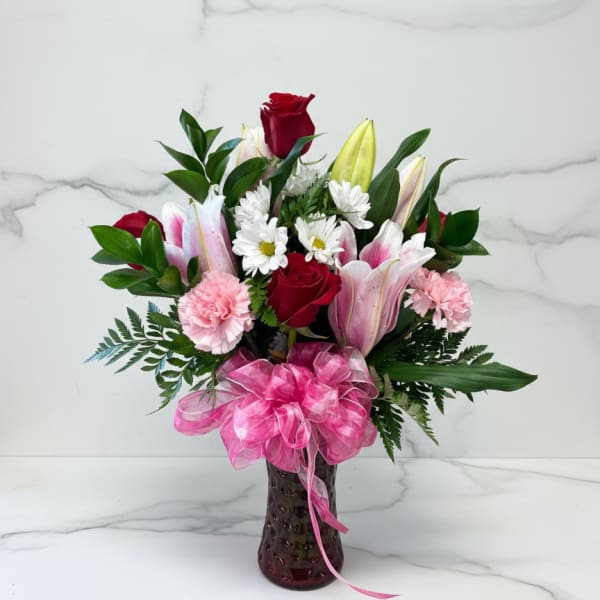 Bouquet of red roses, pink lilies, and white daisies in a vase with a pink bow