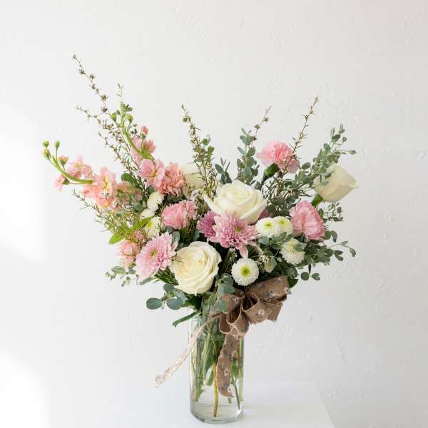 Pink and white flower arrangement in a glass vase with a burlap bow