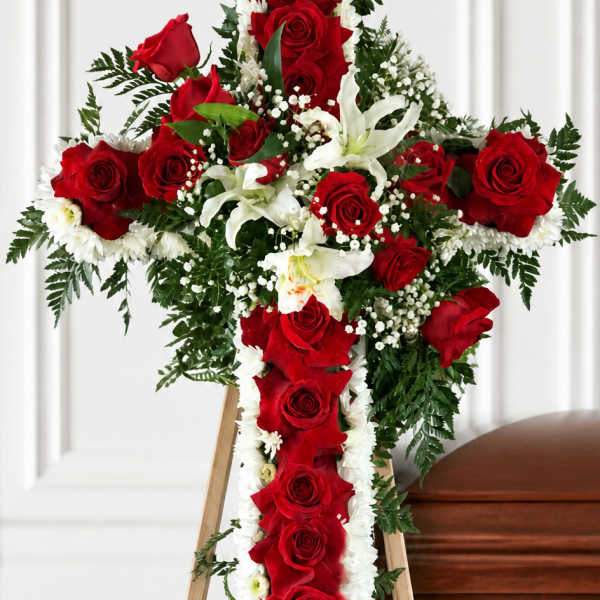 Red and white floral cross on a wooden easel beside a casket