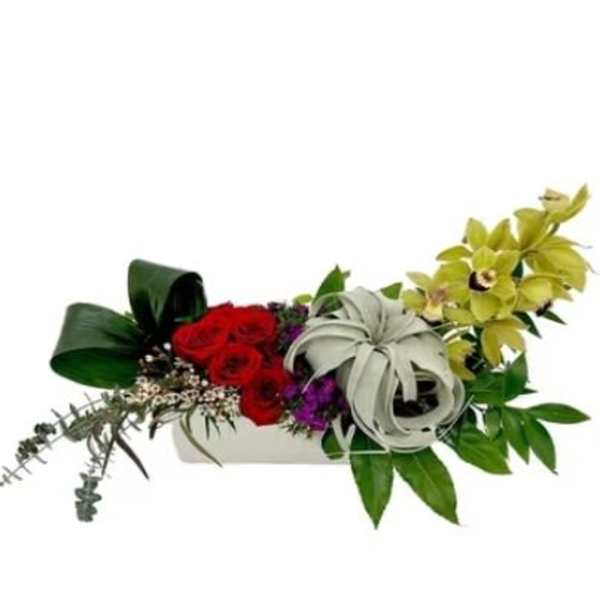 Arrangement of red roses with pale orchids in a white container