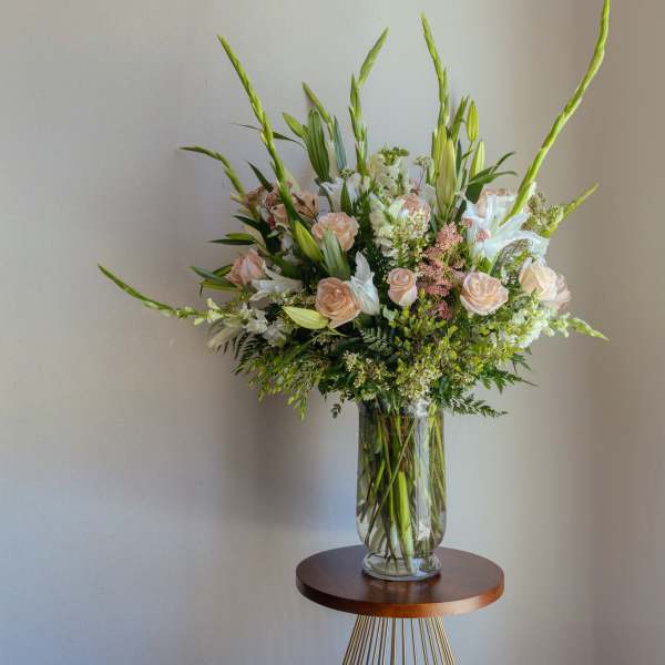 Tall bouquet of pale roses, white lilies, and greenery in a clear glass vase