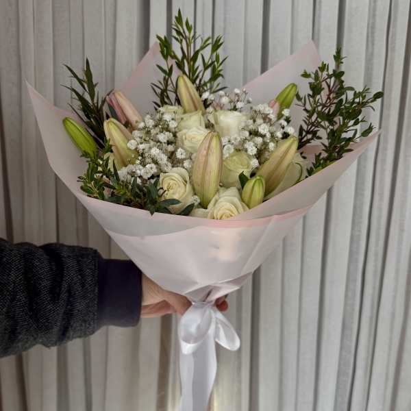Handheld bouquet of white roses and lily buds wrapped in pale pink paper