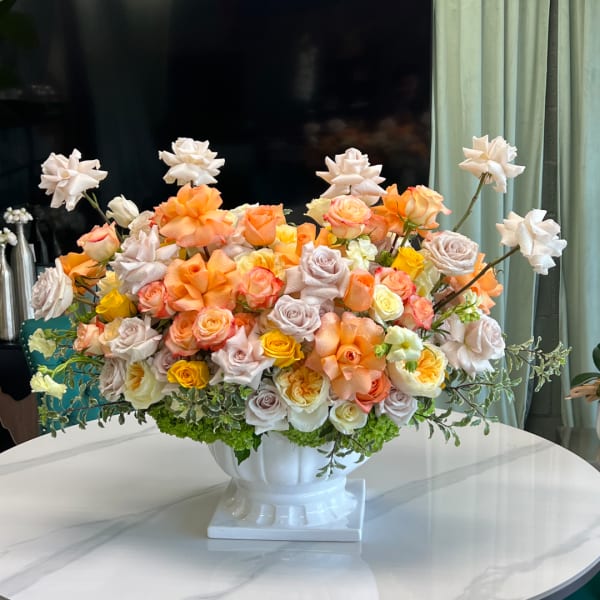 Peach and cream rose arrangement in a white pedestal vase