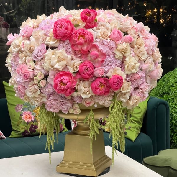 Large pink and cream floral arrangement in a gold pedestal vase