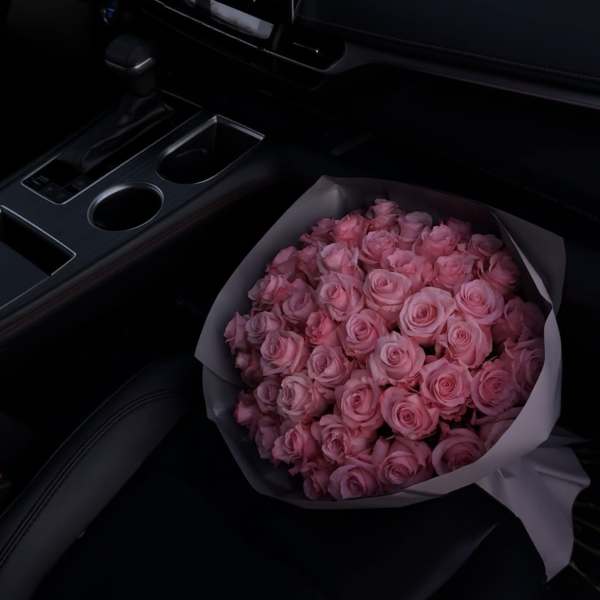Bouquet of pink roses wrapped in white paper on a car seat