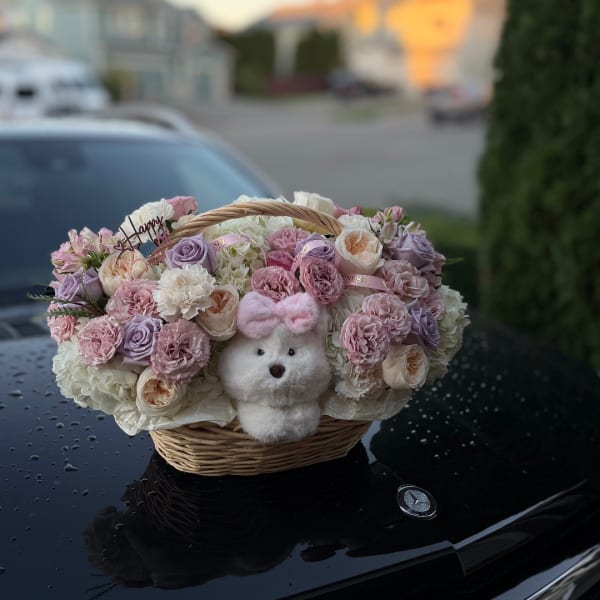 Basket of pastel roses and carnations with a small plush bear