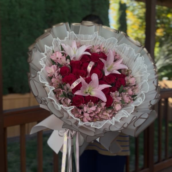 Bouquet of red roses and pink lilies wrapped in white paper