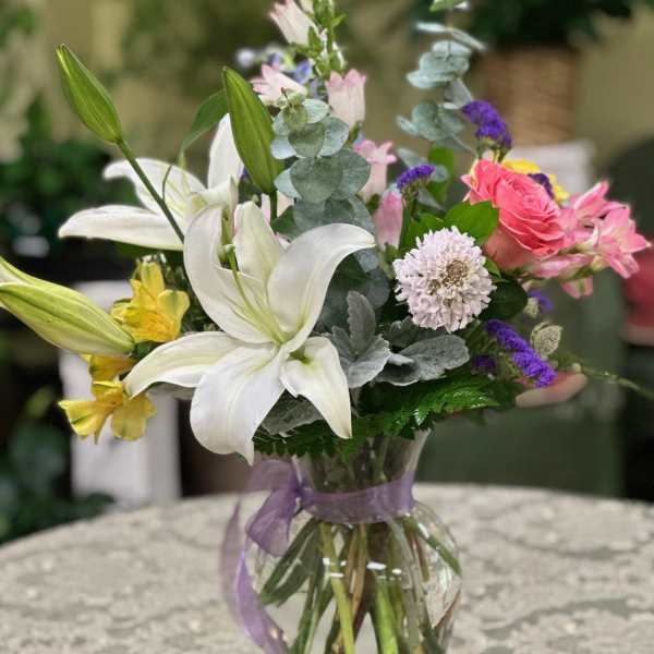 Mixed bouquet with white lilies, pink roses, and purple accents in a glass vase