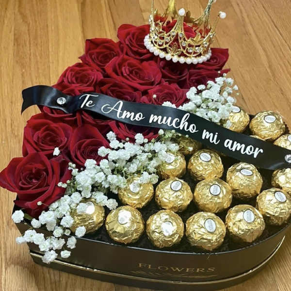 Red roses in a heart-shaped box with gold chocolates and a crown topper