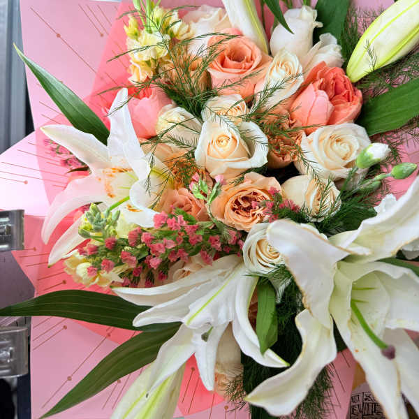 Bouquet of white lilies and peach roses wrapped in pink paper