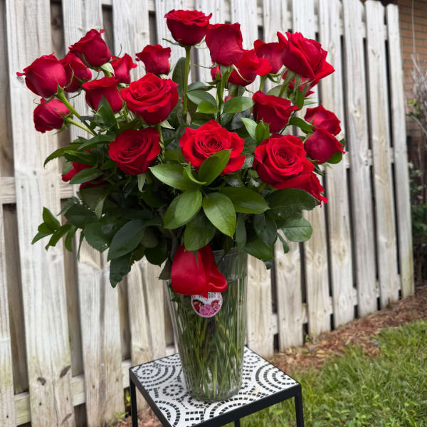 Red roses arranged in a clear glass vase with a red ribbon
