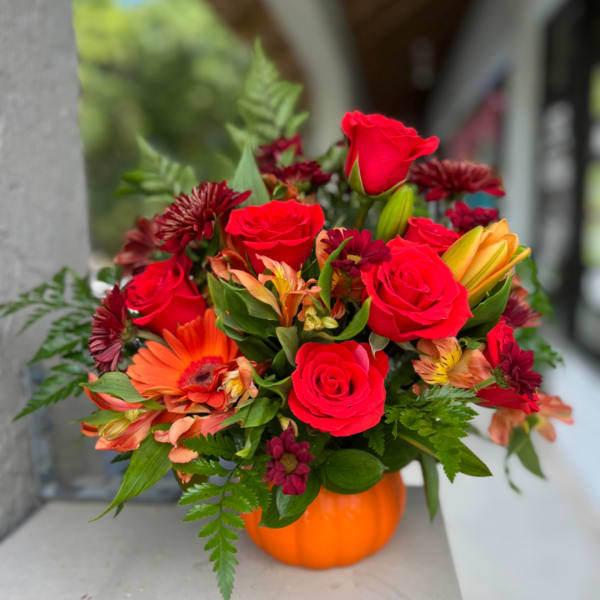 Red roses and mixed flowers arranged in an orange pumpkin vase