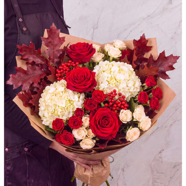 Bouquet of red roses, cream hydrangeas, and red leaves in brown paper