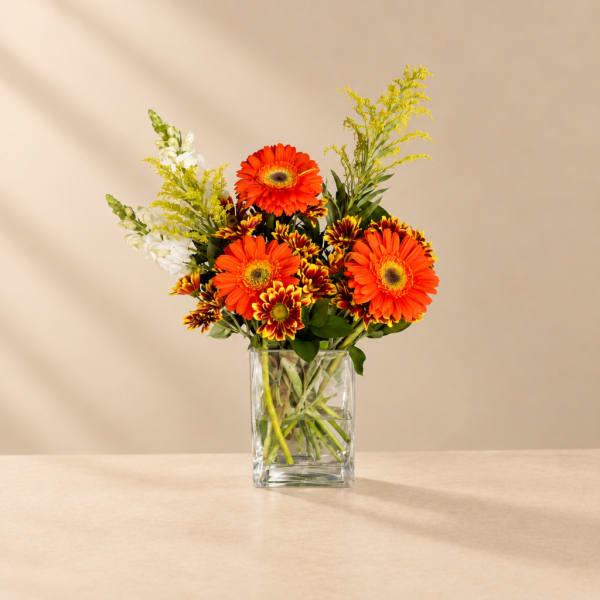 Orange gerbera daisies and mixed blooms in a clear glass vase