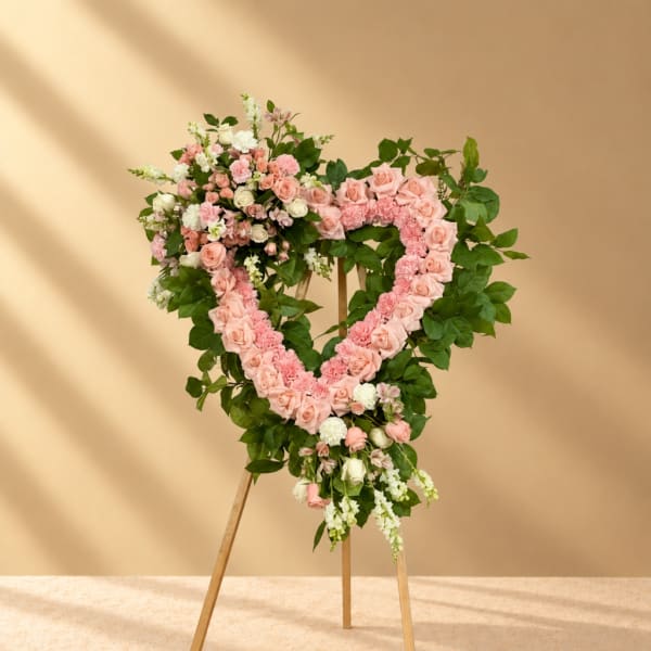 Heart-shaped floral wreath of pink and white roses on a wooden stand