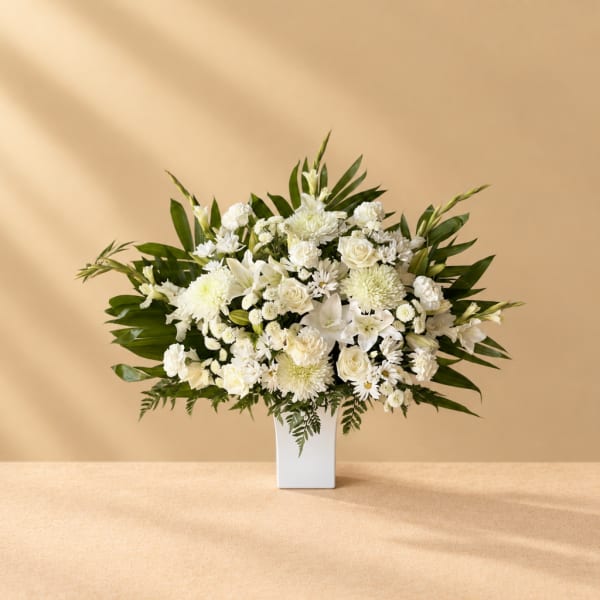 White floral arrangement in a tall white vase with green foliage