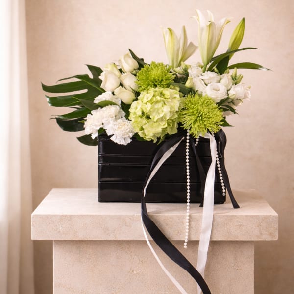 White and green flower arrangement with lilies and roses in a black box with long ribbons