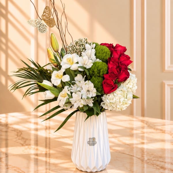 Red roses and white lilies in a white vase with green pompons