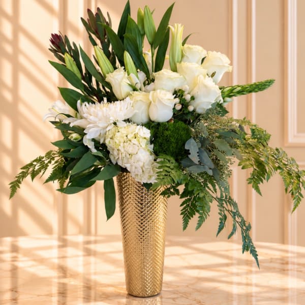 White floral arrangement in a gold textured vase with lush greenery