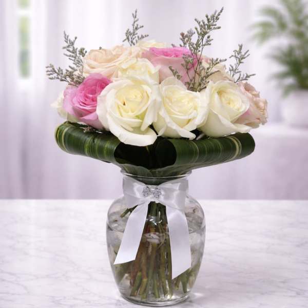 Pink and white roses arranged in a glass vase with a white ribbon