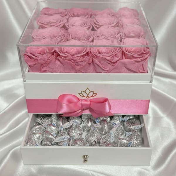 Pink roses in a clear gift box above silver-wrapped chocolates