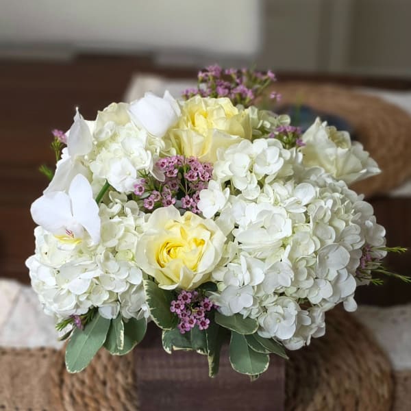 White hydrangea and pale yellow roses in a square vase with small pink accents