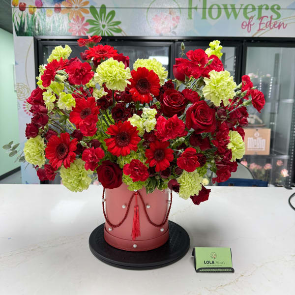 Red and lime-green floral arrangement in a pink hatbox