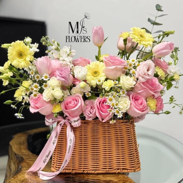 Pink and yellow mixed flower arrangement in a wicker basket with ribbon