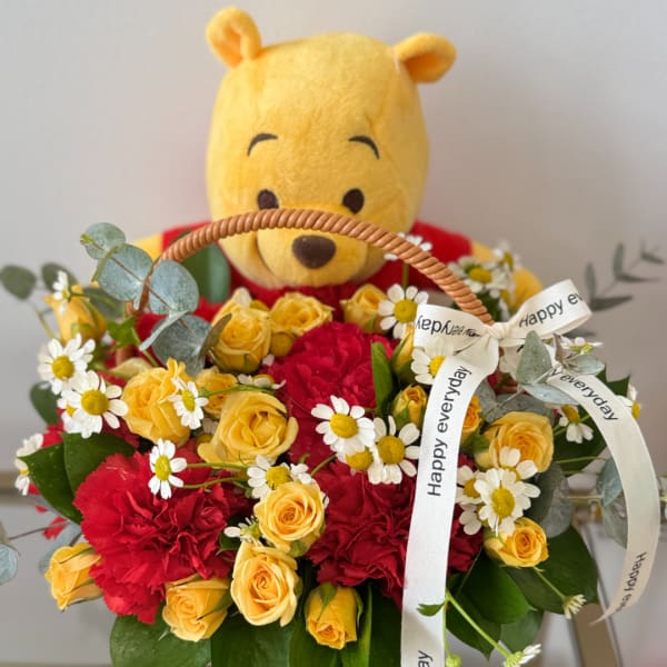 Winnie the Pooh plush in a basket with yellow roses and red carnations