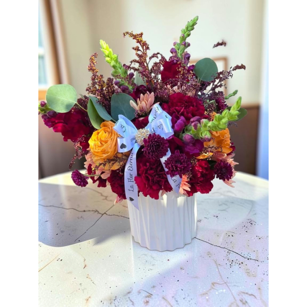 Mixed bouquet in a white ribbed vase with red, yellow, and purple flowers