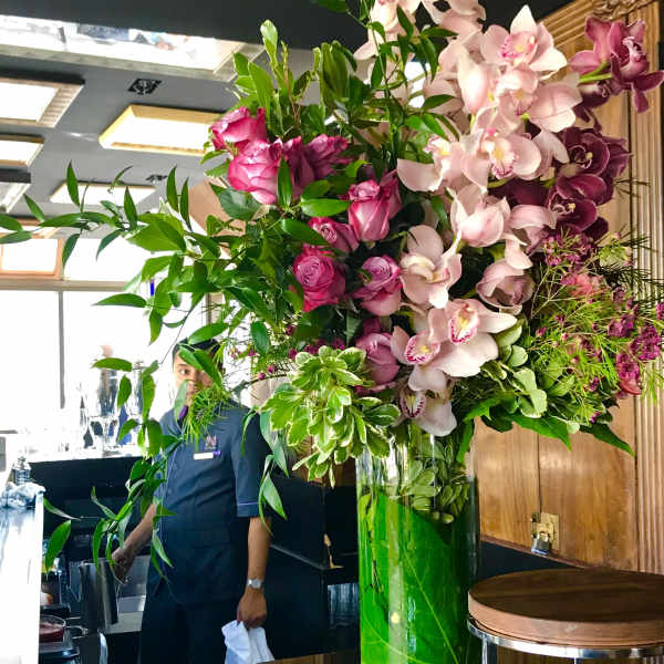 Tall floral arrangement with pink orchids and roses in a glass vase