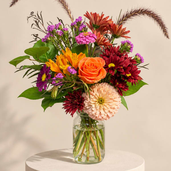 Mixed bouquet of orange, red, and pink flowers in a glass vase