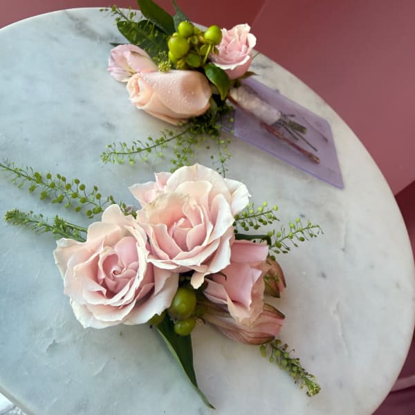 Two pale pink rose boutonnieres with green accents on a marble surface