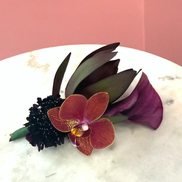 Purple orchid boutonniere with dark leaves and a black accent flower
