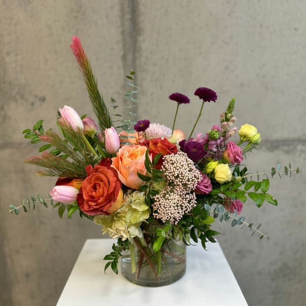 Mixed bouquet in a clear glass vase with roses, tulips, and purple blooms