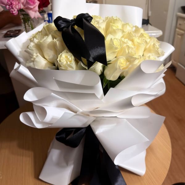 Bouquet of pale yellow roses wrapped in white paper with a black ribbon