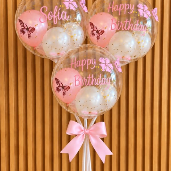 Three pink birthday balloons with butterfly prints and a ribbon bow