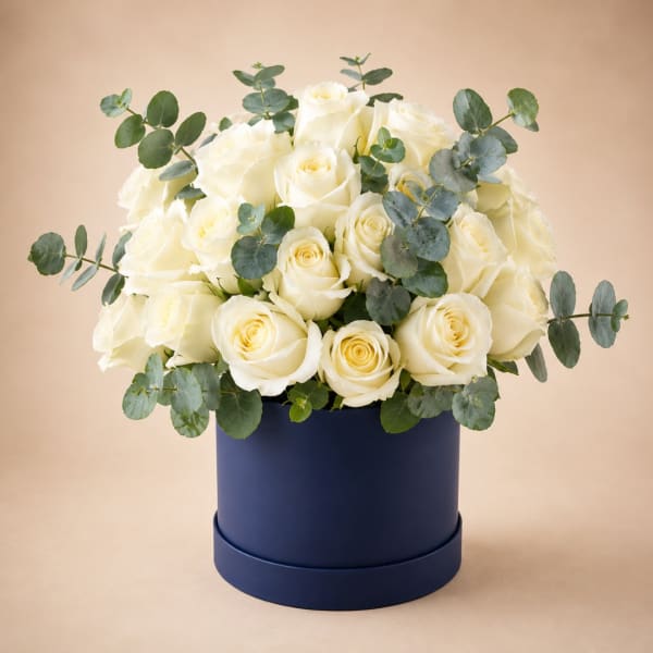 White roses arranged in a navy round box with eucalyptus