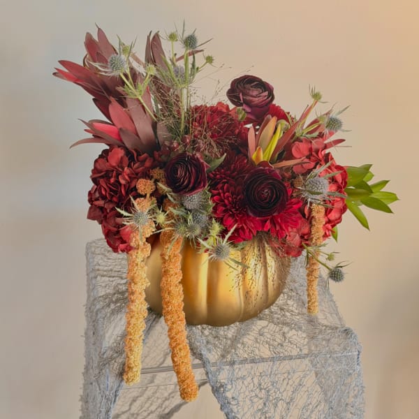 Deep red floral arrangement in a gold pumpkin-shaped vase with trailing blooms